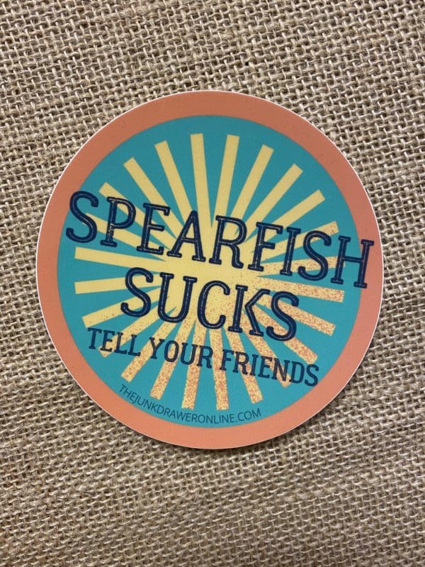 Spearfish Sucks Tells your Friends text above a yellow light symbol on teal background with an orange border.