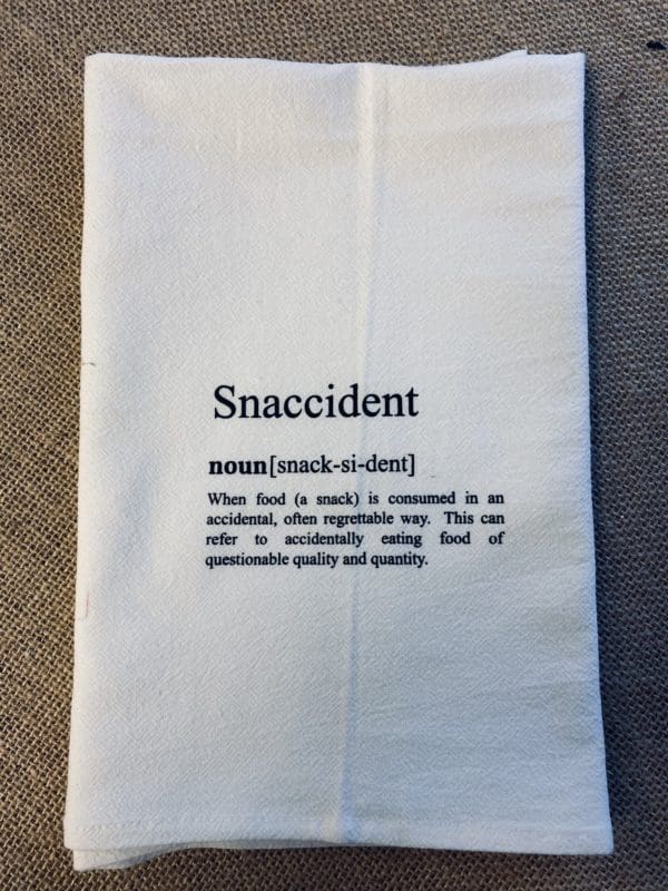 Custom towel with Snaccident text and definition below it explaining when food is consumed in an accidental way
