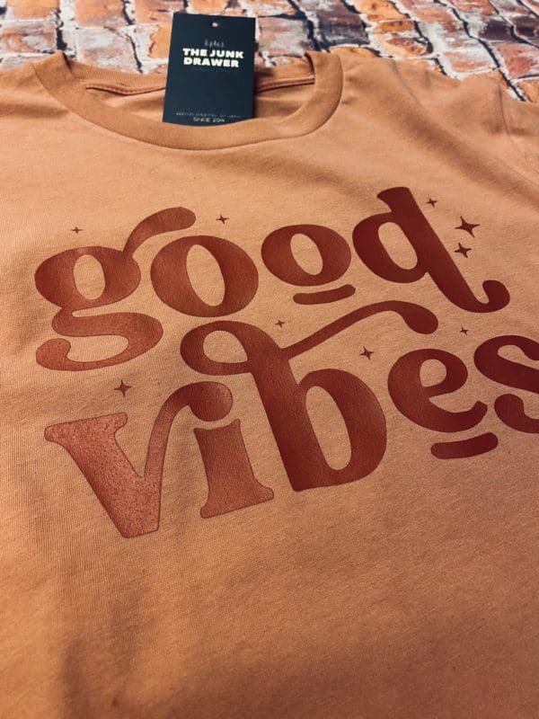 Angled close up of dark red good vibes text on a orange long sleeve t-shirt