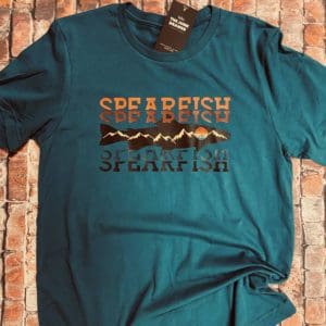 Green T-Shirt with Spearfish text with a orange to black gradient split with a fish design with mountains and a sun within