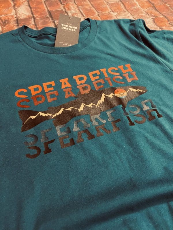 Green T-Shirt with Spearfish text with a orange to black gradient split with a fish design with mountains and a sun within
