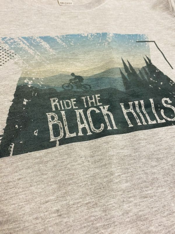 Close up view of the ride the black hills t-shirt design with a rider on mountain bike going over stylized hills