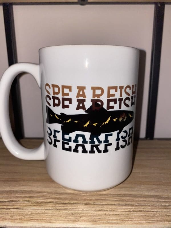 Custom mug with Spearfish text with a orange to black gradient split with a fish design with mountains and a sun within